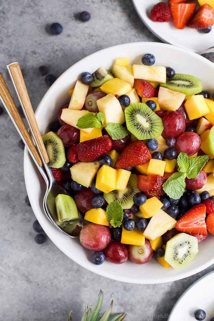 white bowl filled with fruits how to make salad kiwi strawberries blueberries grapes mango pineapple mint leaves