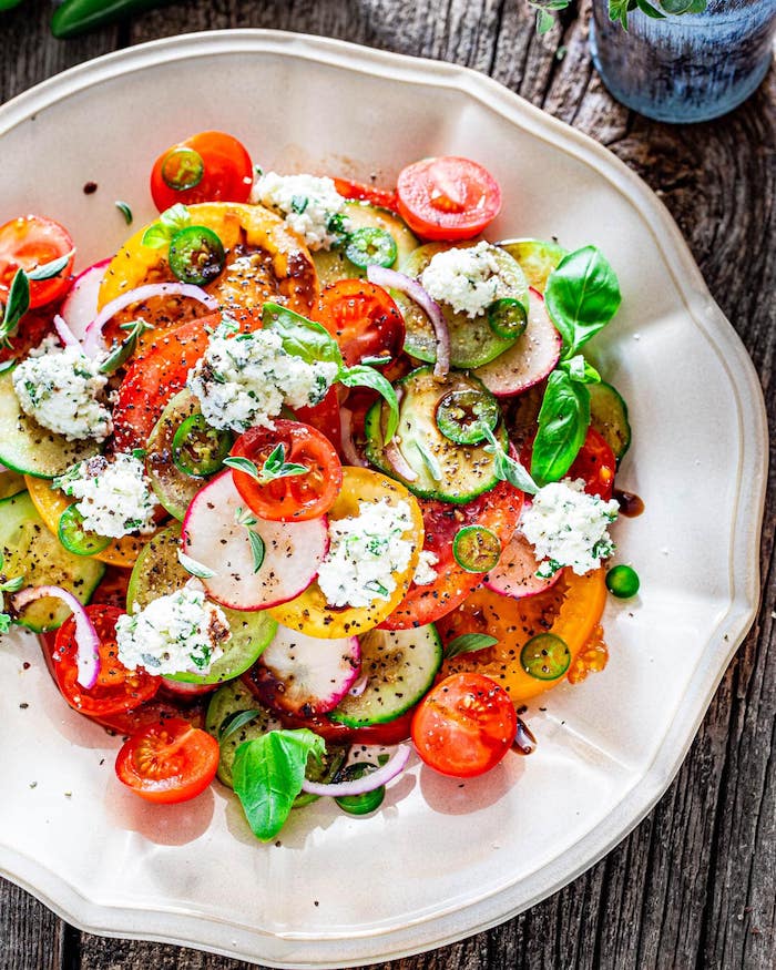 white plate with different types of salads ricotta salad with tomatoes cucumbers peppers turnip basil leaves for garnish