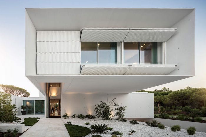 white two storey modern house low maintenance landscaping ideas white gravel in front with grass and bushes tiled pathway leading to the front door