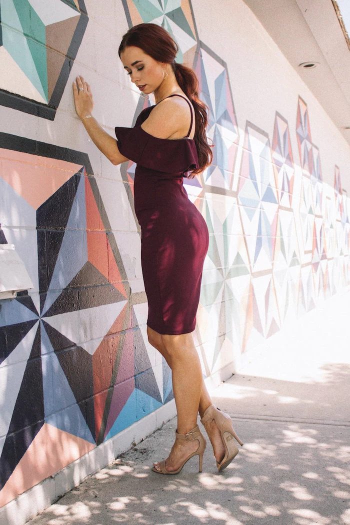 woman leaning on a wall wearing dark burgundy dress beach wedding guest dresses nude sandals with long wavy hair in low ponytail