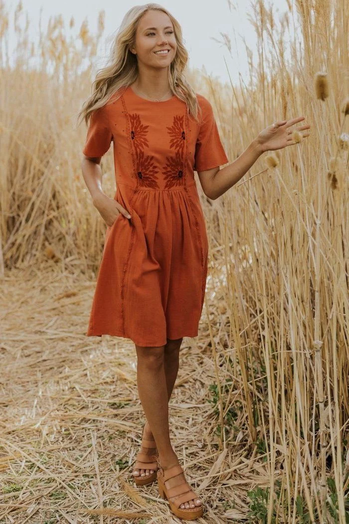 woman with long blonde wavy hair standing in a field flowy dresses wearing orange dress brown leather sandals