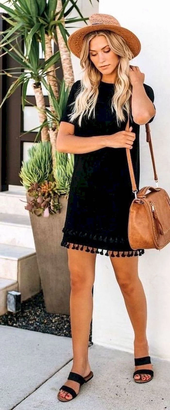 woman with long wavy hair wearing black dress and sandals womens dresses brown hat and leather bag