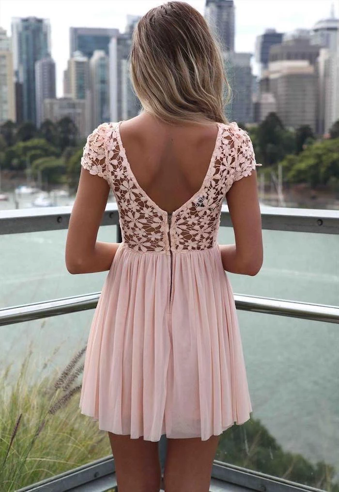 woman with long wavy hair wearing short pink dress with lace top summer dresses with sleeves standing on a balcony