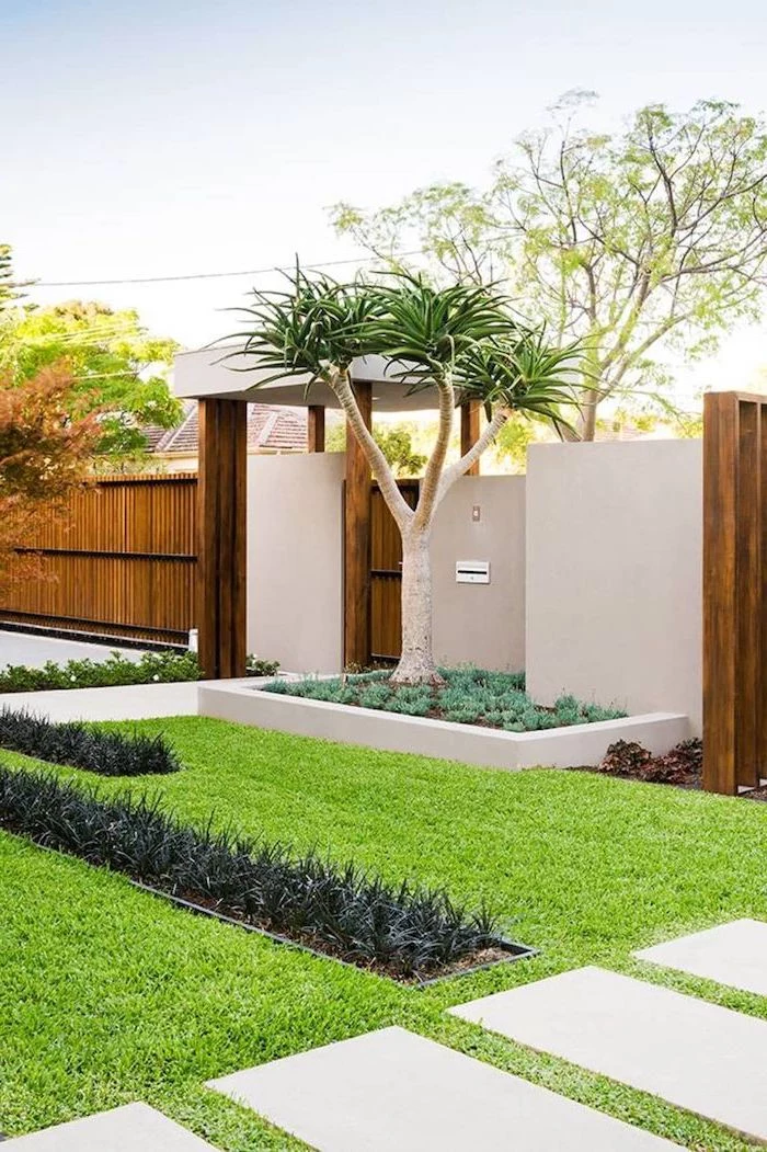 wooden fence with gate tree planted right next to it simple landscaping ideas tiled pathways surrounded by grass and flower beds