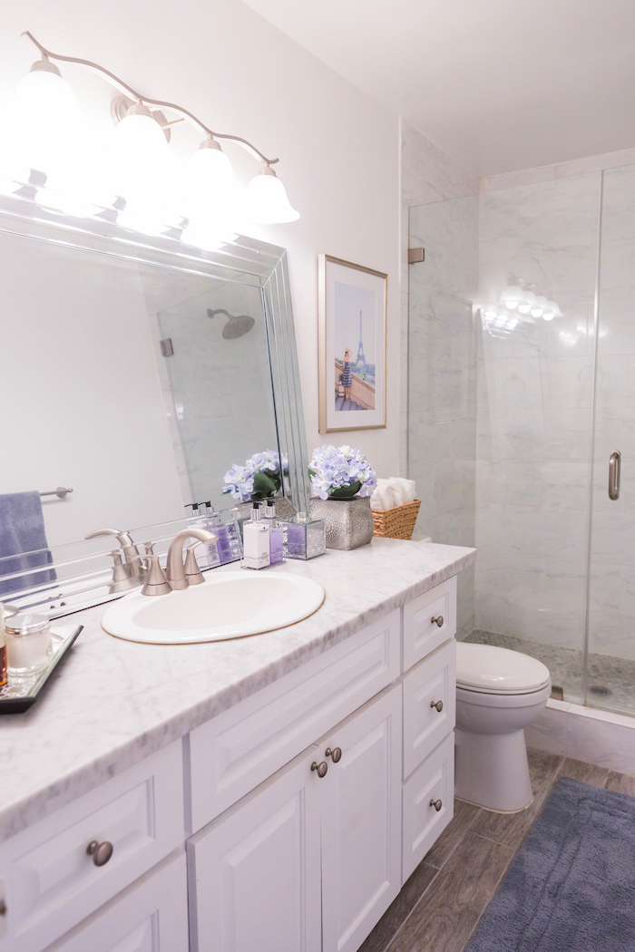 bathroom decor pictures marble countertop on white cabinets mirror leaning on white wall lights above it blue carpet on wooden floor