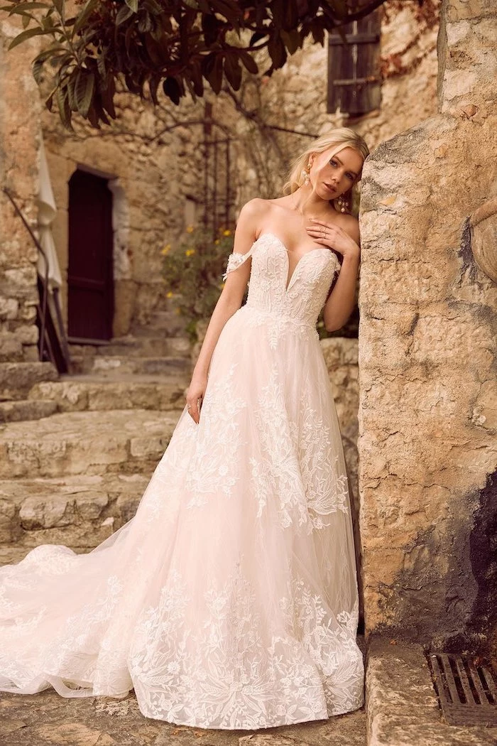 blonde woman leaning on stone wall short sleeve wedding dress wearing dress made of lace and tulle