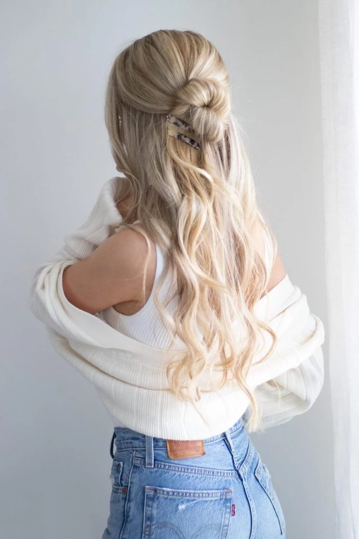 blonde woman with long wavy hair half uf it in a bun cool hairstyles for girls wearing white top cardigan jeans