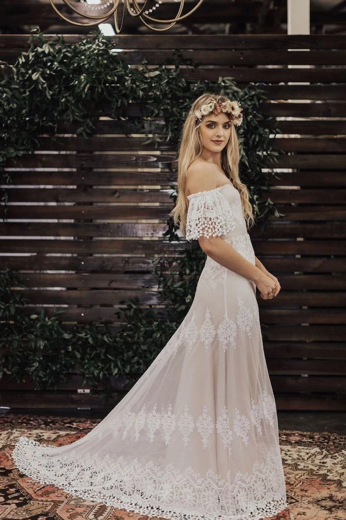 blonde woman with long wavy hair long sleeve lace wedding dress wearing lace dress standing in front of wooden backdrop