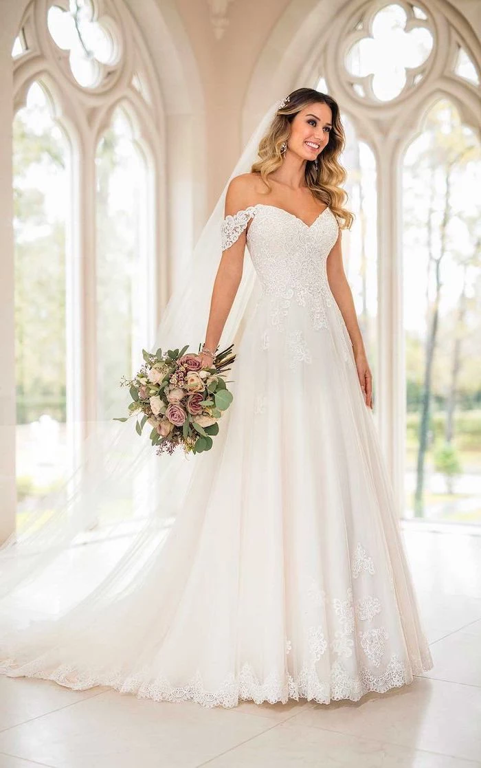 blonde woman with long wavy hair wearing ball gown wedding dress made of tulle and lace holding a bouquet