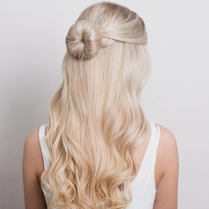 blonde woman with long wavy hair wearing white top easy hairstyles for long hair half of the hair tied in a small bun