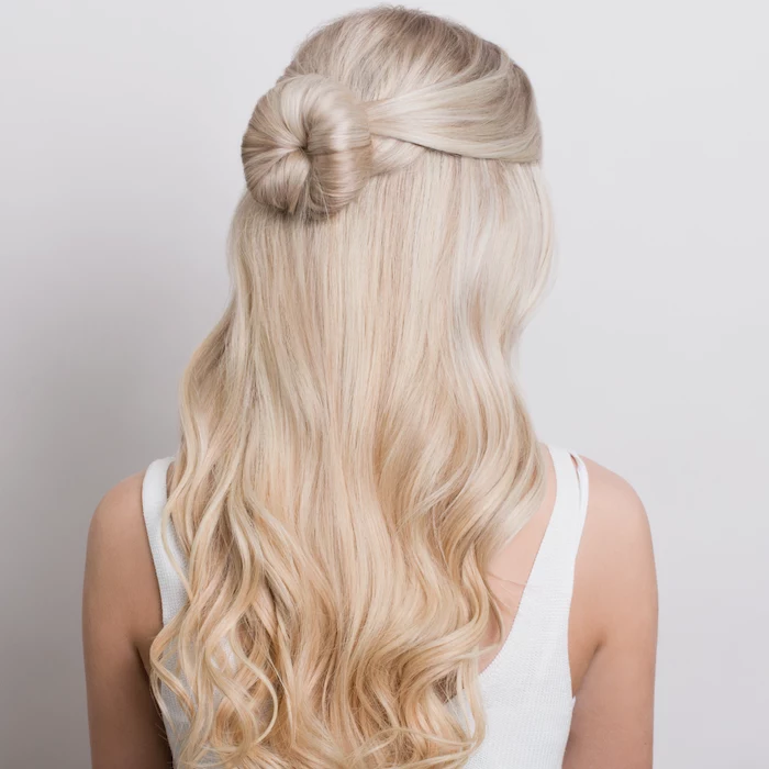 blonde woman with long wavy hair wearing white top easy hairstyles for long hair half of the hair tied in a small bun