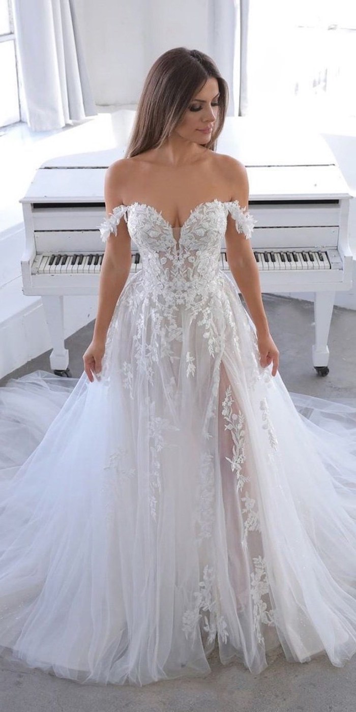 brunette woman standing in front of vintage piano beaded wedding dresses wearing white dress made of lace and tulle