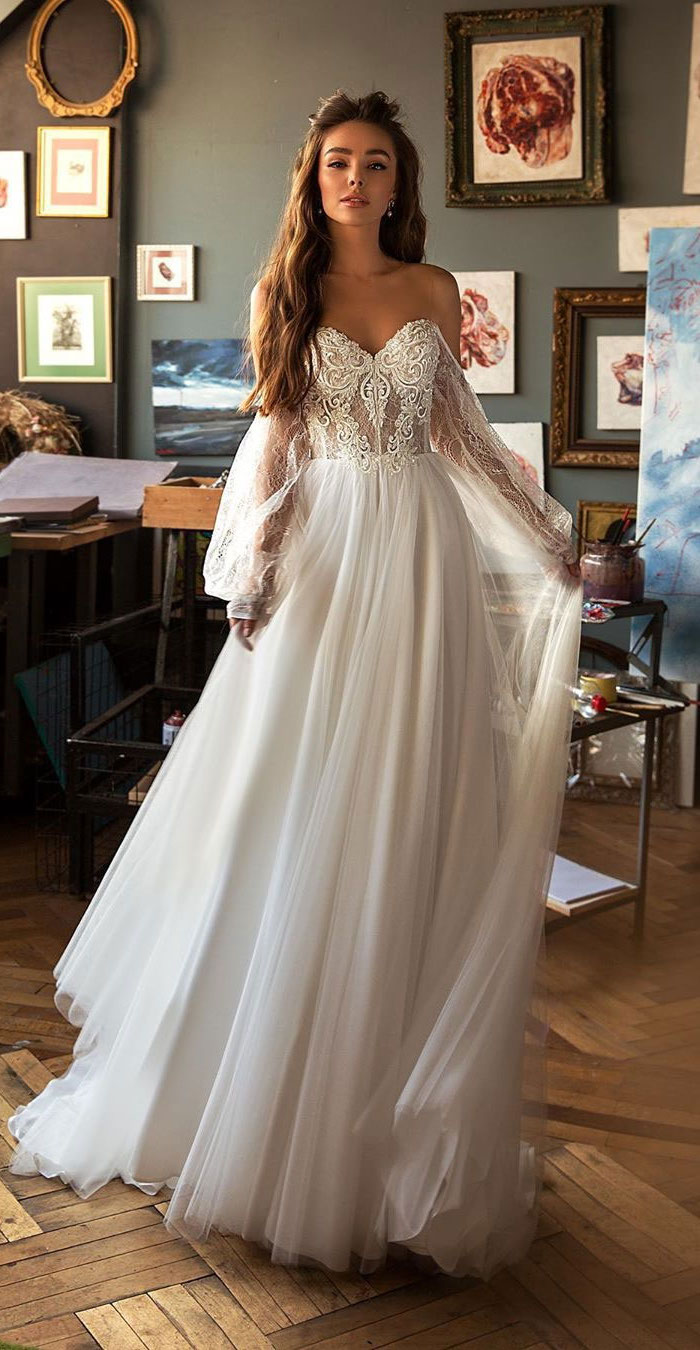 brunette woman with long wavy hair wearing tulle dress with lace long sleeves and corsette off the shoulder mermaid wedding dress