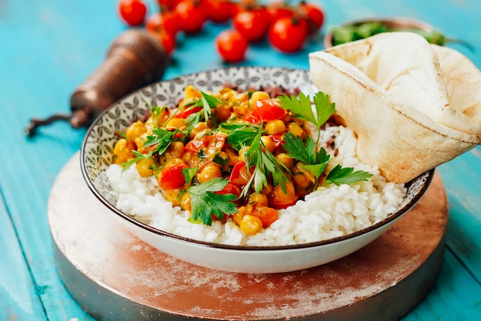 chickpea curry being served with white rice and naan bread in black and white bowl how to cook chickpeas blue wooden surface