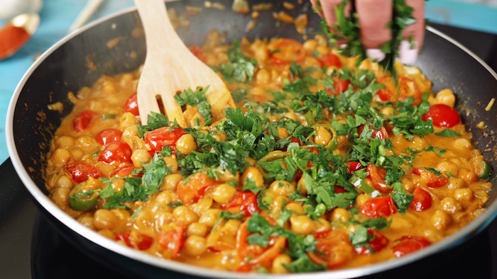 chickpea curry cooking in saucepan with wooden spatula chickpea recipe chopped parsley added to saucepan
