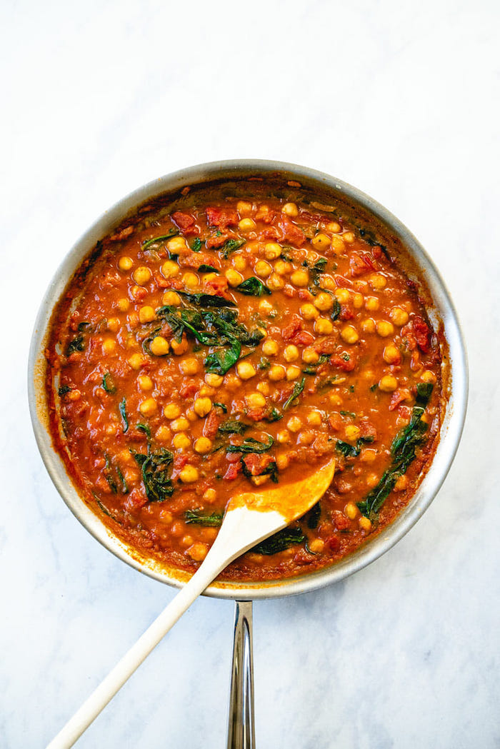 chickpea curry with spinach easy chickpea recipes cooked in skillet placed on marble surface stirred with wooden spoon