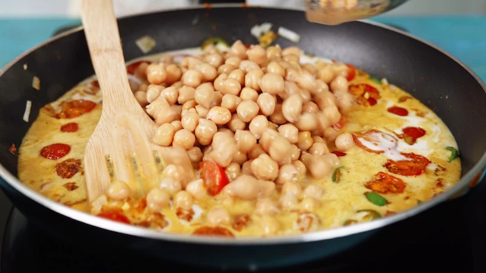 chickpeas being added into saucepan chickpea recipe milk cherry tomatoes jalapeno onion cooking in saucepan with wooden spatula