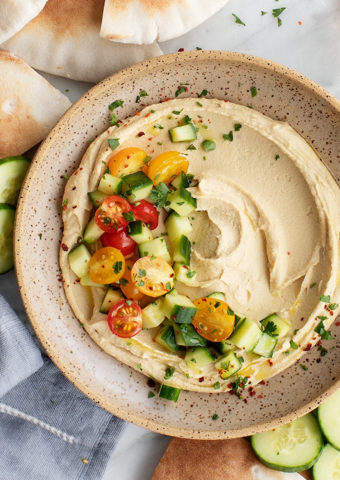 creamy hummus garnished with chopped cucumbers cherry tomatoes parsley canned chickpea recipes placed in ceramic bowl
