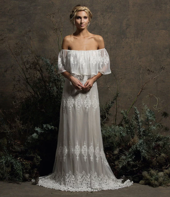 fit and flare wedding dress blonde woman with hair in low updo wearing dress made of lace standing in front of dark wall