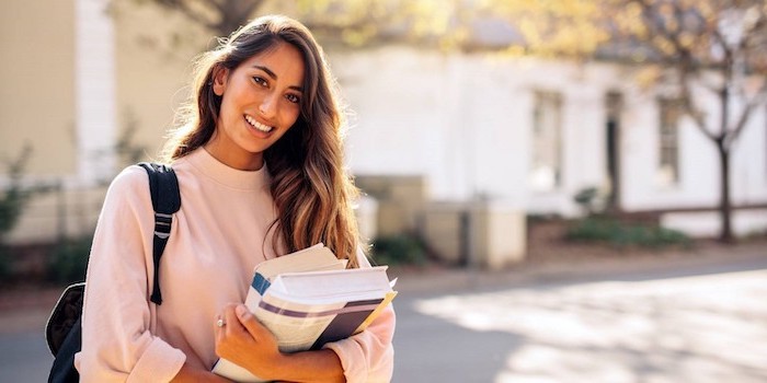 girl with long brown balayage hair holding textbooks easy hairstyles for school wearing pink sweatshirt