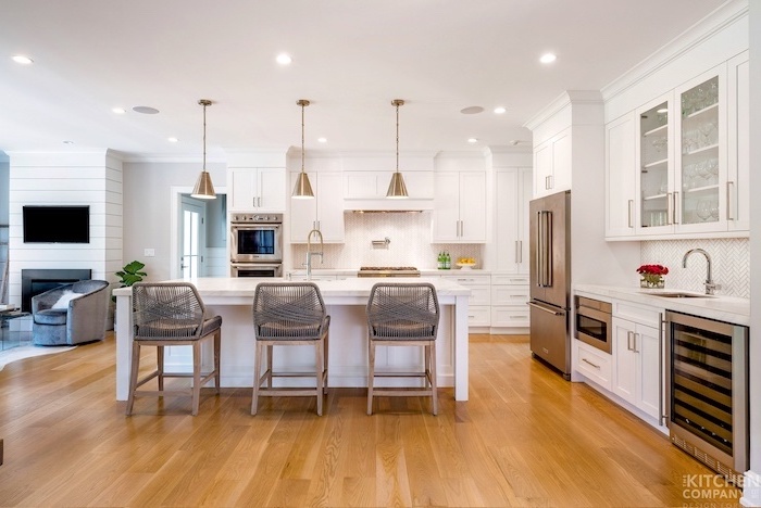 gray stools next to white kitchen island white farmhouse kitchen white cabinets white countertops wooden floor white tiles backsplash