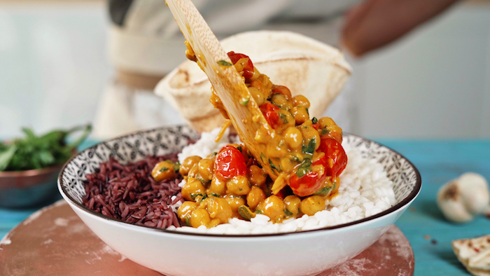 how to cook chickpeas chickpea curry being poured on top of white and brown rice with wooden spatula