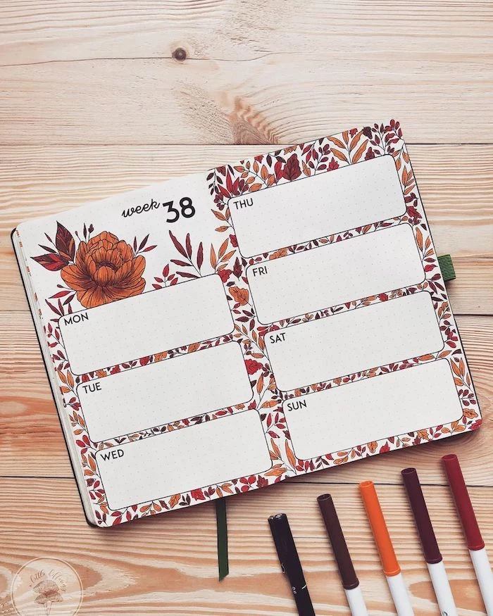 open notebook with weekly spread with orange flowers leaves drawn on it bullet journal weekly spread placed on wooden surface