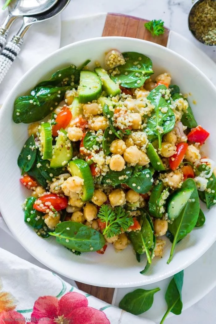 what are chickpeas salad with spinach cucumbers cherry tomatoes quinoa onion inside white ceramic bowl