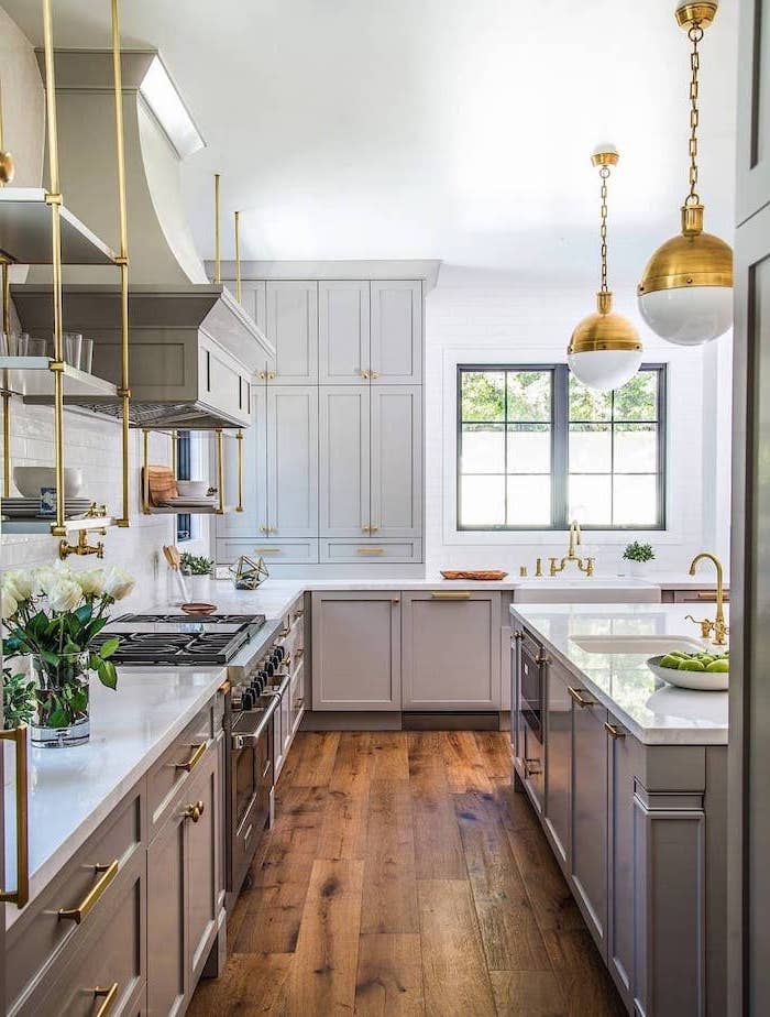 white farmhouse kitchen dark wooden floor light gray cabinets open shelving with brass fixtures white subway tiles backsplash