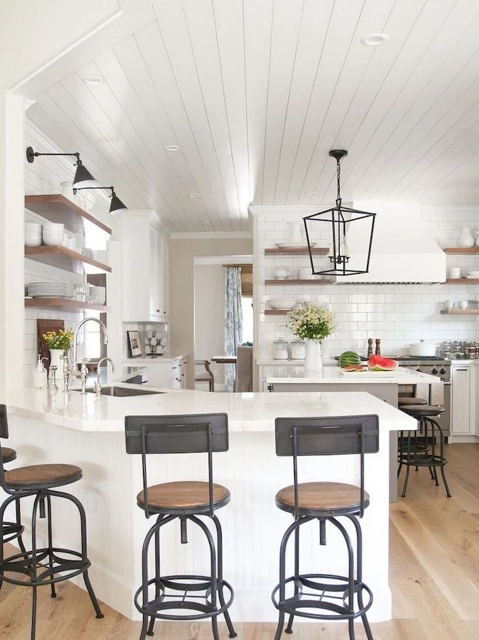 white wooden ceiling white tiles on the walls farmhouse kitchen decor white countertops and cabinets black metal chairs