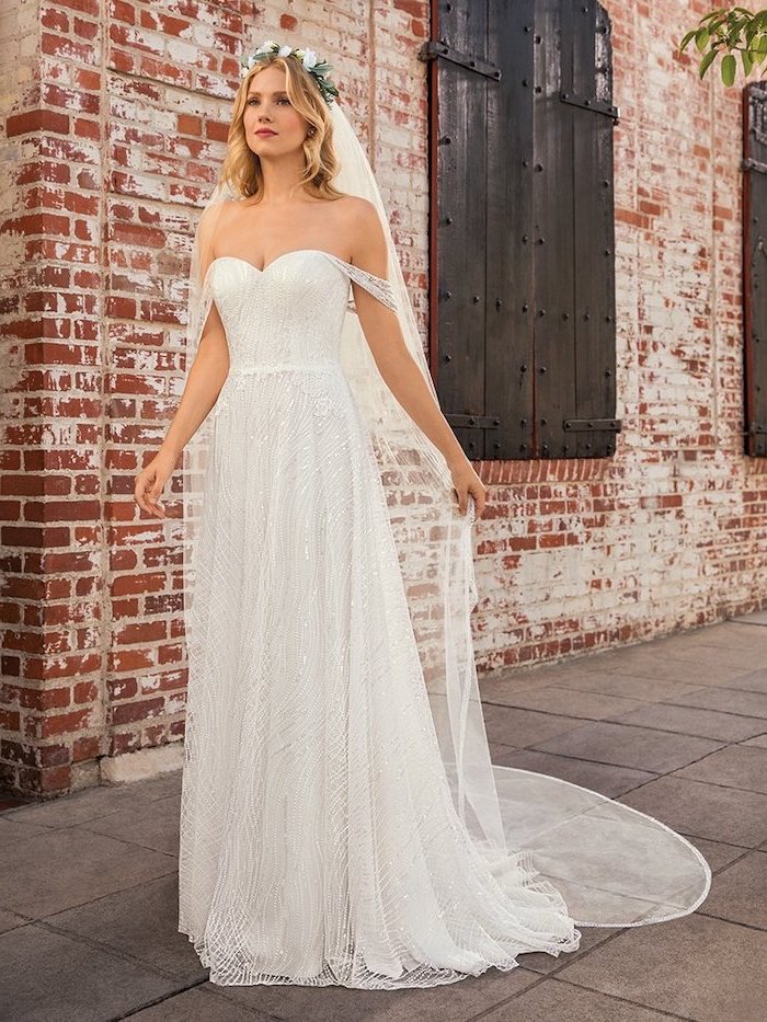 woman standing on side walk in front of brick wall long sleeve lace wedding dress wearing dress made of tulle long veil