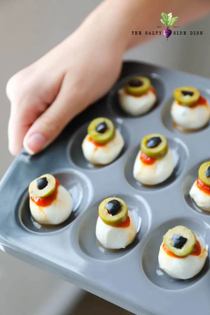 baby mozzarella with salsa and olives arranged in gray muffin baking tray halloween party treats