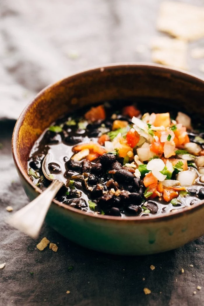 black bean soup inside brown ceramic bowl instant pot one pot meals garnished with parsley chopped tomatoes and peppers