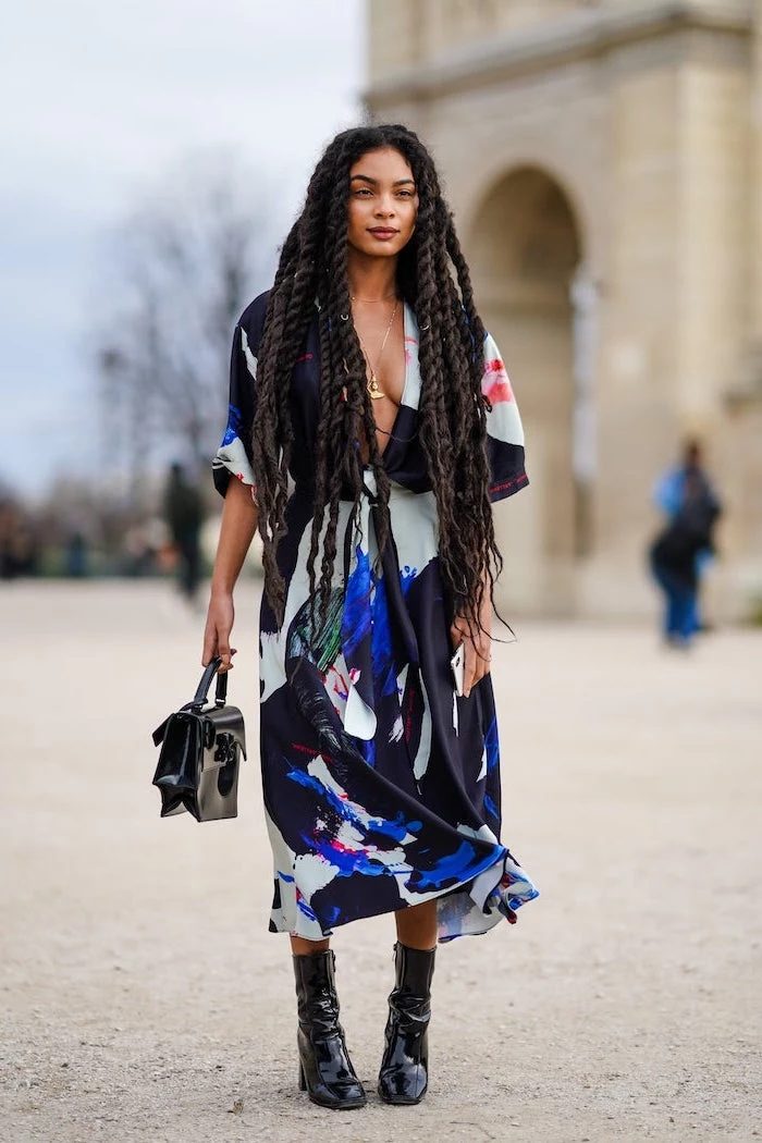 black boots and bag midi dress with abstract colorful rint worn by woman with long black dreads cute trendy outfits standing on the sidewalk