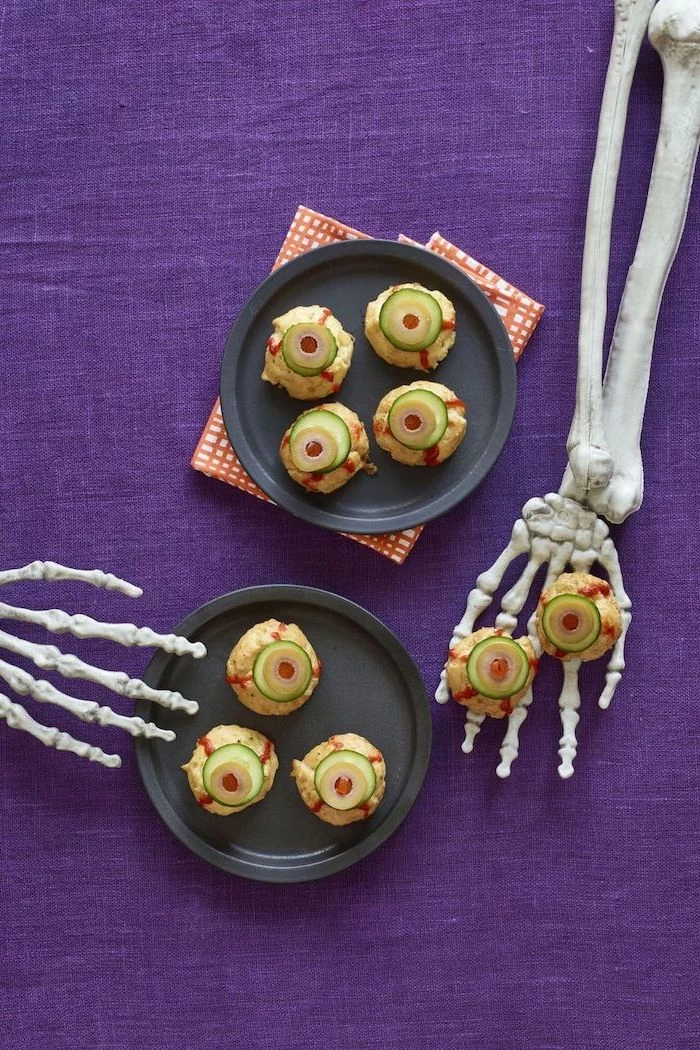 black plates with monster eye bites inside placed on purple table cloth halloween appetizers skeleton hands on the table