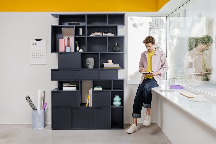 black wooden bookcase with shelves and drawers in different shapes bookcase ideas man standing next to it reading a book