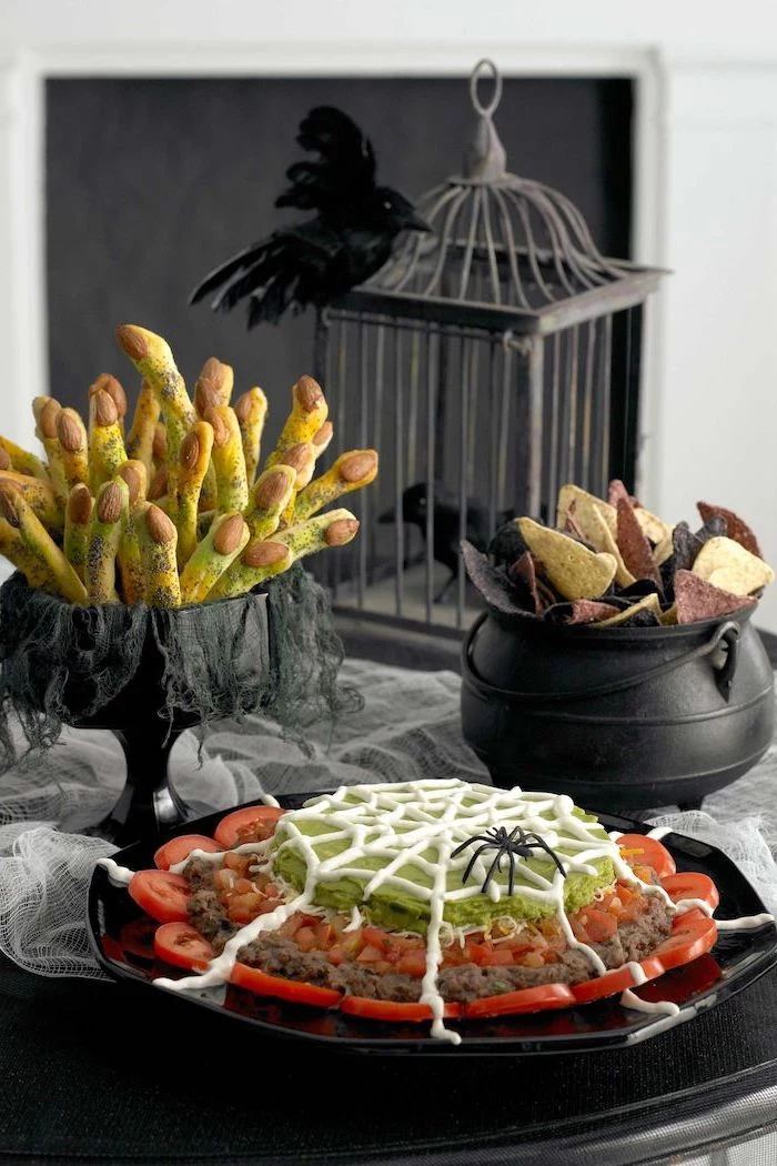 black wooden table decorated with white tulle halloween appetizers black tray with tomatoes meat guacamole dip tortilla chips in black cauldron breadsticks