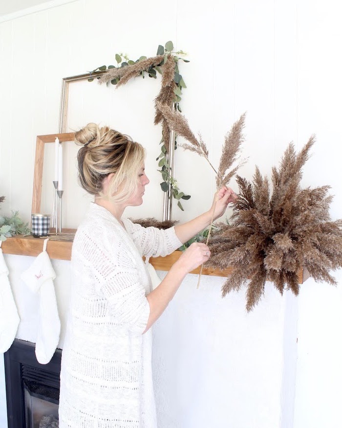 blonde woman decoratingher mantel for christmas wearing white cardigan where to buy pampas grass two candles and stockings