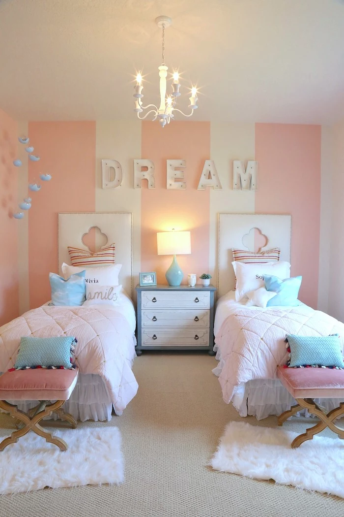 blue throw pillows on two single beds night stand between them cozy teenage girl room pink white striped wall dream written on it