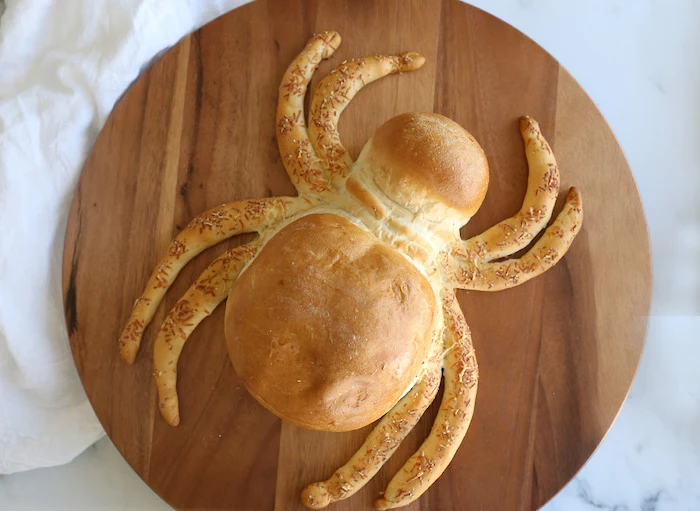 bread baked in the shape of a large spider easy halloween appetizers placed on wooden cutting board placed on white surface