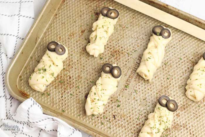 breadsticks with dough wrapped around them as mummies olives for eyes halloween party appetizers baked in baking tray