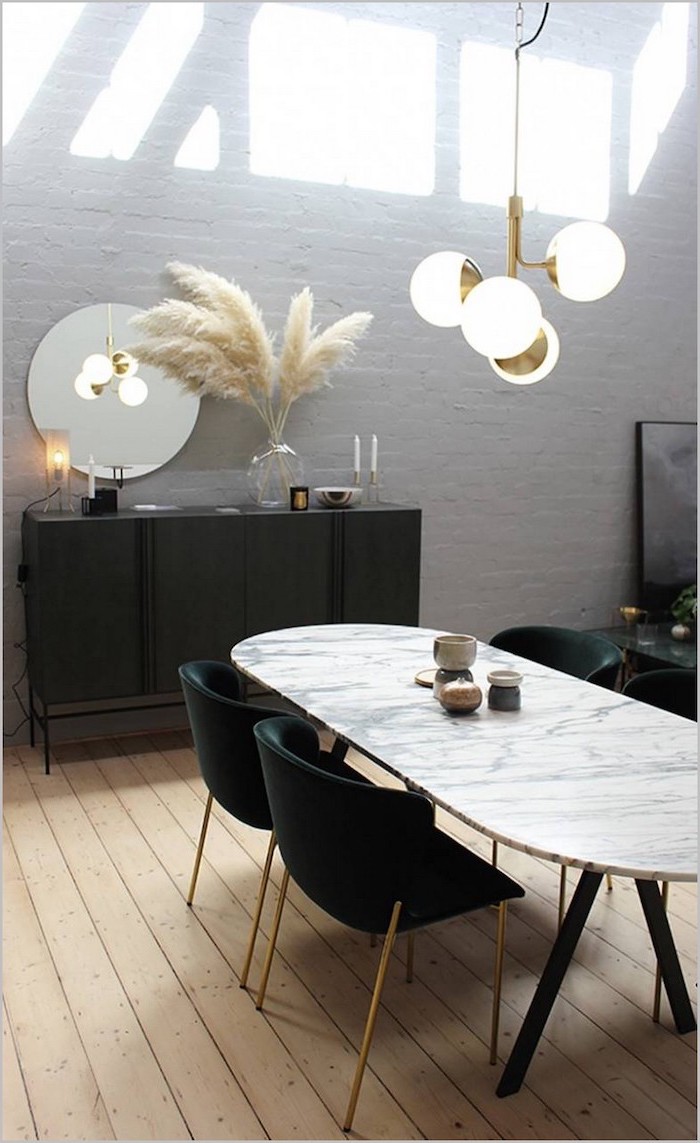 brick accent wall behind black cupboard with a glass vase with dried pampas grass inside marble dining table black chairs