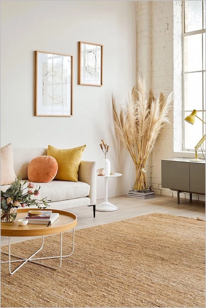 brick accent wall in living room with white sofa wooden table wooden floor with large carpet dried pampas grass inside glass vase in the corner