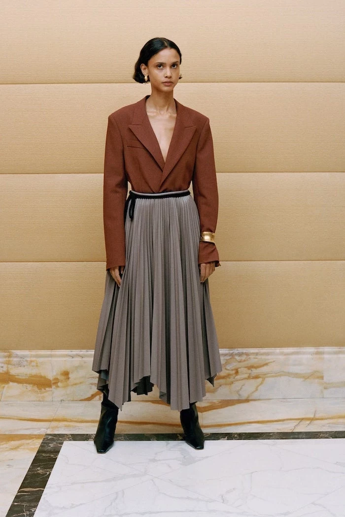 brown blazer tucked into long gray pleated skirt worn with black boots fall fashion trends worn by woman with short black hair