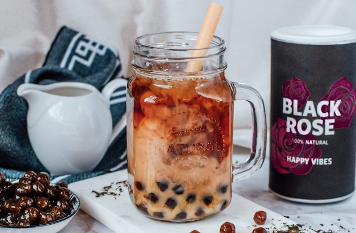 bubble tea recipe boba tea poured inside glass with handle and plastic straw placed on white board tea and jug of milk in the background