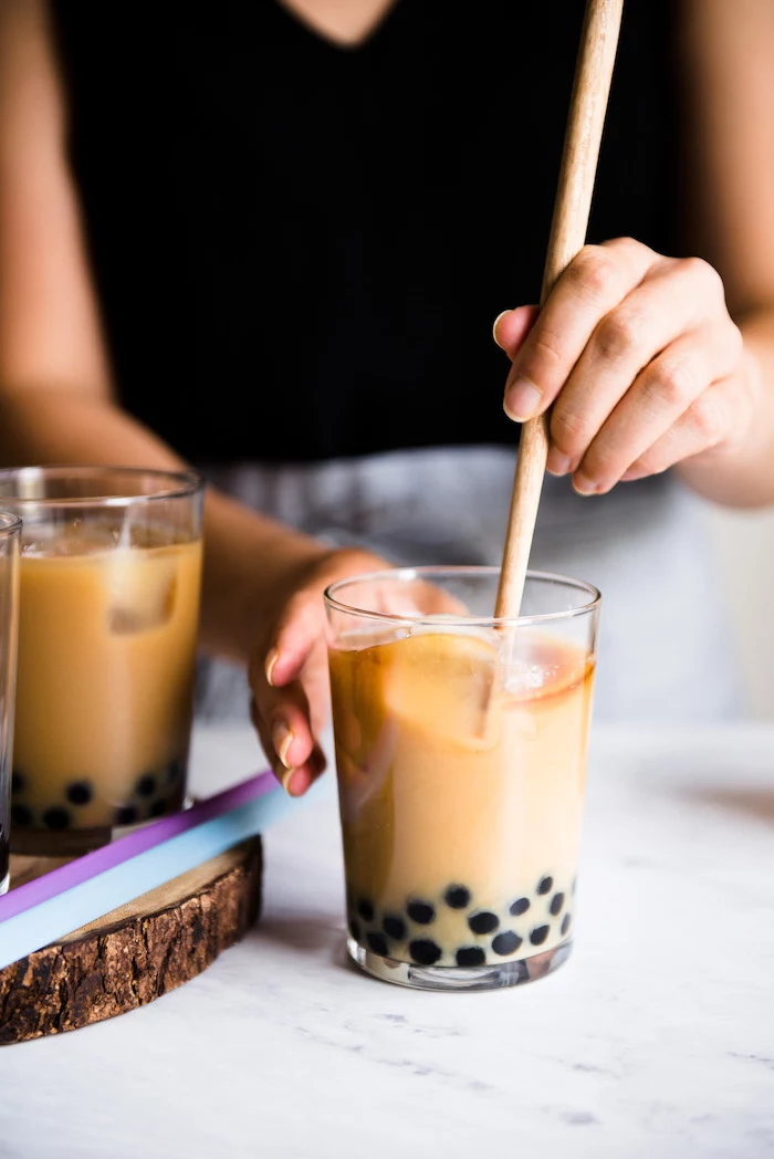 bubble tea step by step milk and boba being stirred with wooden spoon how to make milk tea glass placed on marble surface