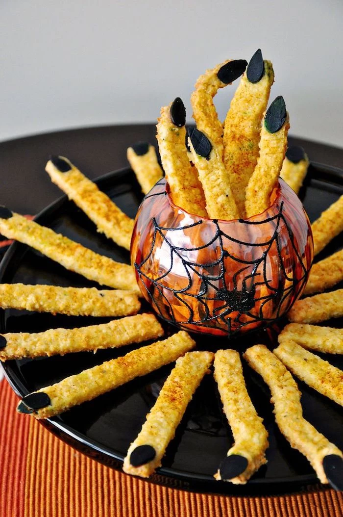 cheddar sticks with breadcrumbs placed on black plate arranged around red bowl halloween themed food black nuts for nails