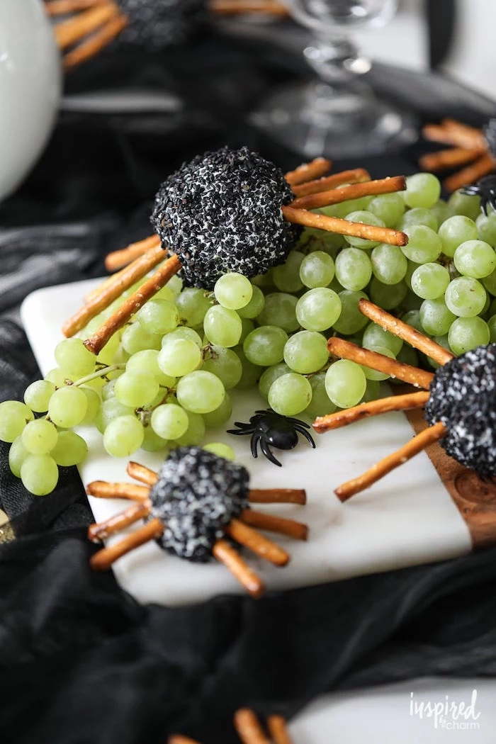 cheeseballs with pretzels as spiders halloween party appetizers placed on wooden cutting board with grape