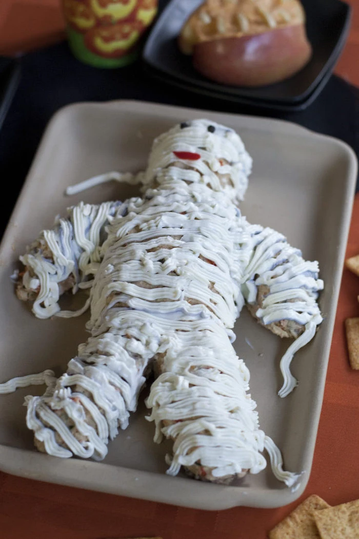 cheesy mummy recipes halloween party snacks placed on gray baking tray orange table cloth crackers on the side
