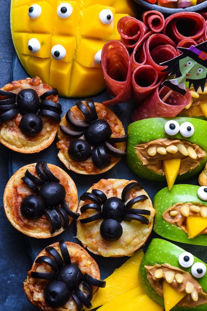 crackers with olives arranged as spiders apples with peanut butter salami mango halloween party treats arranged on black platter